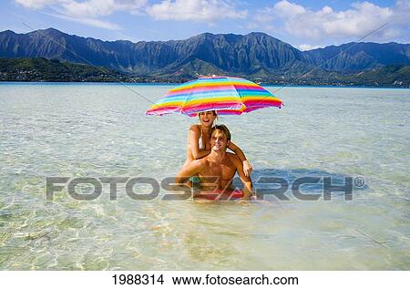 Picture - Hawaii, Oahu, Kaneohe, Couple Under A Brightly Colored Umbrella In Crystal Clear Water At The Sandbar Or Dissapearing Island. Fotosearch