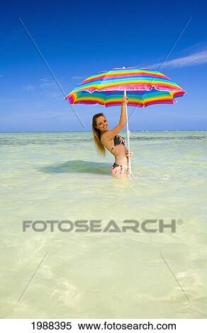 Stock Photography - Hawaii, Oahu, Kaneohe, Woman Standing Under A Brightly Colored Umbrella In Crystal Clear Water At The Sandbar Or Dissapearing Island. Fotosearch