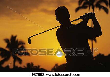 Stock Image - Hawaii, Oahu, Ko Olina Golf Course, Silhouette Of Man Swinging Golf Club, Orange Sunset Sky.. Fotosearch