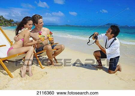 Stock Image - Hawaii, Oahu, Lanikai, A beachboy takes a picture of a young couple on the beach.. Fotosearch