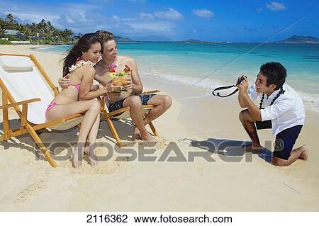 Stock Image - Hawaii, Oahu, Lanikai, A beachboy takes a picture of a young couple on the beach.. Fotosearch
