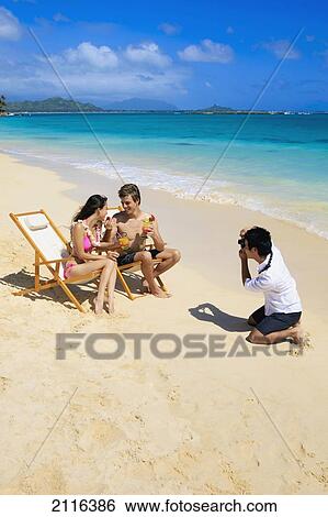 Stock Photograph - Hawaii, Oahu, Lanikai, A beachboy takes a picture of a young couple on the beach.. Fotosearch