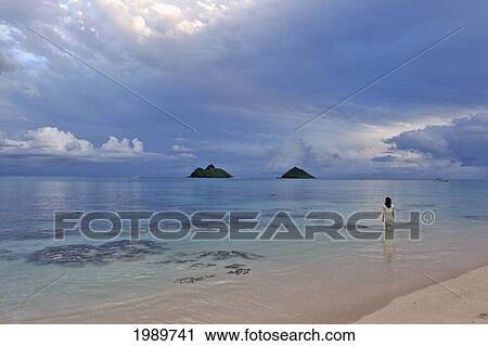 Stock Image - Hawaii, Oahu, Lanikai, A Woman Wades In The Water At The Beach At Dusk.. Fotosearch