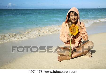 Stock Image - Hawaii, Oahu, Lanikai, Attractive Young Woman On The Beach With Sunflower.. Fotosearch