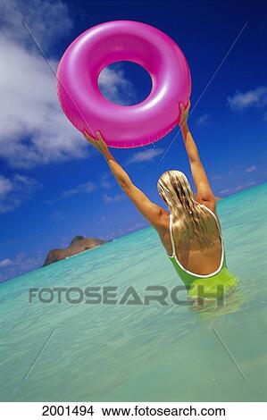 Picture - Hawaii, Oahu, Lanikai Beach, Back View Of Woman In Bathing Suit Holding Pink Inner Tube Over Her Head. Fotosearch