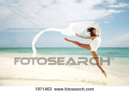 Stock Image - Hawaii, Oahu, Lanikai Beach, Beautiful Female Ballet Dancer Leaping Into Air On Beach With White Flowing Fabric.. Fotosearch