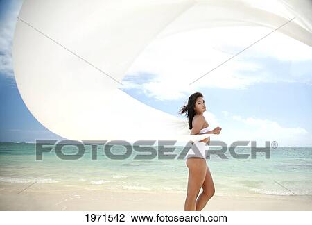 Stock Image - Hawaii, Oahu, Lanikai Beach, Beautiful Young Woman On Beach With White Fabric Blowing In The Wind.. Fotosearch