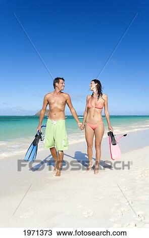 Stock Image - Hawaii, Oahu, Lanikai Beach, Couple Walking Along Seashore With Snorkel Gear.. Fotosearch