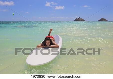 Stock Image - Hawaii, Oahu, Lanikai Beach, Girl Floating On Surfboard, Mokulua Islets In Background.. Fotosearch