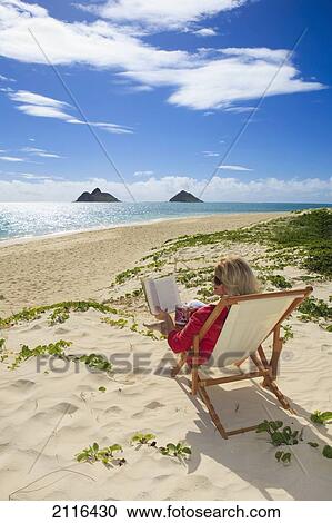 Stock Image - Hawaii, Oahu, Lanikai Beach, Woman reading a book on white sandy beach.. Fotosearch