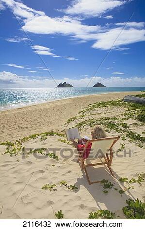 Stock Image - Hawaii, Oahu, Lanikai Beach, Woman reading a book on white sandy beach.. Fotosearch