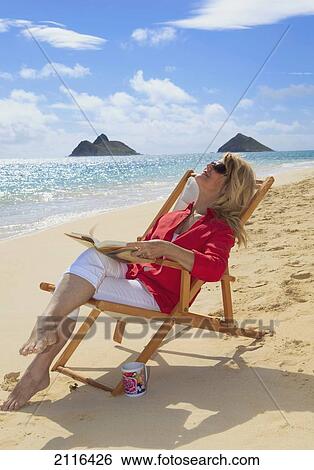 Stock Photograph - Hawaii, Oahu, Lanikai Beach, Woman reads and soaks up sun on white sandy beach.. Fotosearch