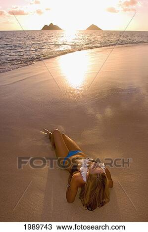 Stock Image - Hawaii, Oahu, Lanikai Beach, Young Women Reclines On The Wet Sand At Sunrise.. Fotosearch