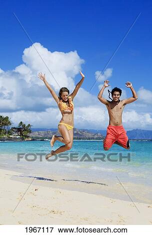 Stock Photo - Hawaii, Oahu, Lanikai Beach, Young Couple Jumping On Beach.. Fotosearch