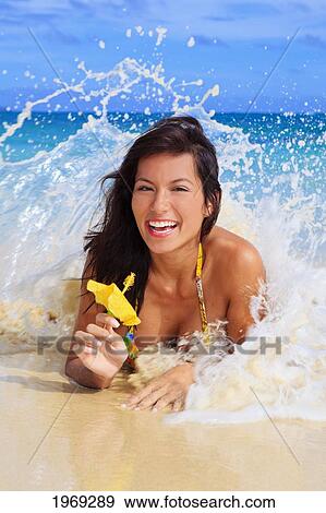 Stock Photo - Hawaii, Oahu, Lanikai, Beautiful Woman On The Beach Holding A Yellow Hibiscus With Wave Crashing On Her.. Fotosearch
