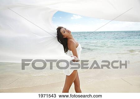 Stock Image - Hawaii, Oahu, Lanikai, Beautiful Young Woman On Beach With White Fabric Blowing In The Wind.. Fotosearch