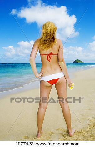 Stock Image - Hawaii, Oahu, Lanikai, Bikini-Clad Girl On Beach Holding Plumeria Flowers, View From Behind.. Fotosearch