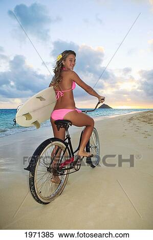 Stock Photography - Hawaii, Oahu, Lanikai, Blond Surfer Girl Holding Surfboard While Riding Bike Along Beach.. Fotosearch