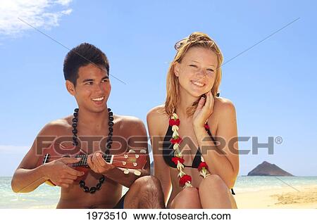 Stock Image - Hawaii, Oahu, Lanikai, Hawaiian Beachboy Plays His Ukulele For A Beautiful Blond Girl.. Fotosearch