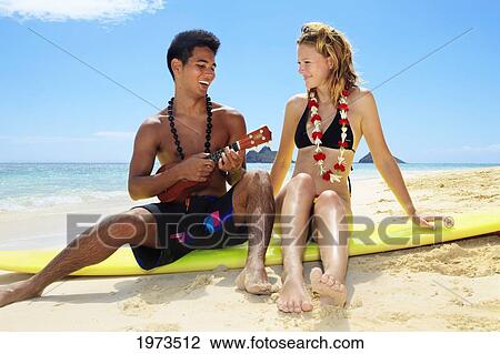 Stock Image - Hawaii, Oahu, Lanikai, Hawaiian Beachboy Plays His Ukulele For A Beautiful Blond Girl.. Fotosearch