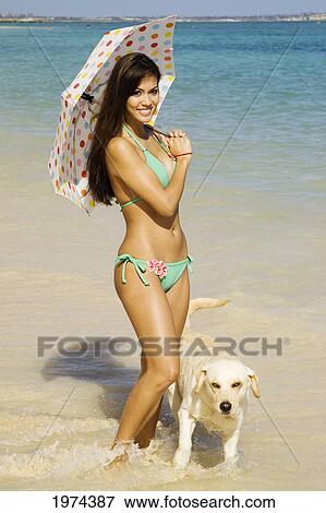 Stock Photo - Hawaii, Oahu, Lanikai, Portrait Of Attractive Young Woman Holding An Umbrella And Walking With Her Dog.. Fotosearch