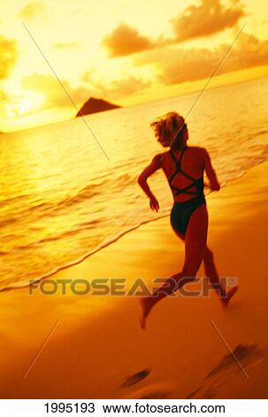 Stock Image - Hawaii, Oahu, Lanikai, Woman Jogging On The Beach At Sunrise.. Fotosearch