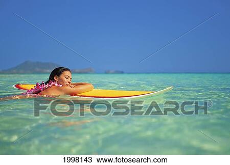 Stock Image - Hawaii, Oahu, Lanikai, Woman Resting Face Of Surfboard While In Ocean With Eyes Closed. Fotosearch