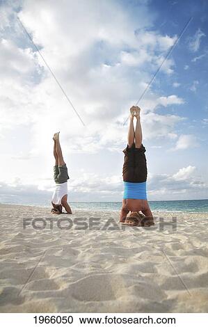 Stock Image - Hawaii, Oahu, Lanikai, Young Couple Doing Yoga, Stay In A Headstand Position On The Beach.. Fotosearch
