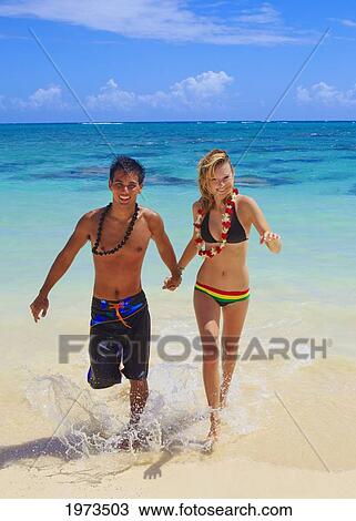 Stock Image - Hawaii, Oahu, Lanikai, Young Couple Running Out Of The Ocean.. Fotosearch