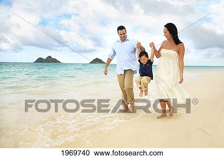 Stock Image - Hawaii, Oahu, Lanikai, Young Family Holding Hands Strolling Along The Beach.. Fotosearch