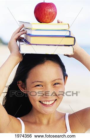 Stock Photograph - Hawaii, Oahu, Lanikai, Young Girl On The Beach Holding A Stack Of Books And An Apple On Her Head.. Fotosearch