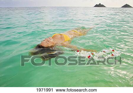 Stock Image - Hawaii, Oahu, Lanikai, Young Woman Floating In Tropical Ocean Water With Lei.. Fotosearch