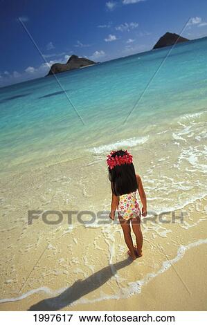 Stock Photo - Hawaii, Oahu, Little Girl With Plumeria Haku Standing In Shoreline Water, Mokulua Islands In Background. Fotosearch