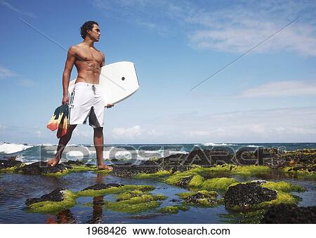 Hawaii, Oahu, Local Bodyboarder Standing On Tidepool Of Rocks Near The Shoreline. View Large Photo Image Stock Photograph - Hawaii, Oahu, Local Bodyboarder Standing On Tidepool Of Rocks Near The Shoreline.. Fotosearch