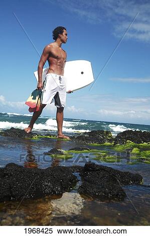 Hawaii, Oahu, Local Bodyboarder Standing On Tidepool Of Rocks Near The Shoreline. View Large Photo Image Stock Photography - Hawaii, Oahu, Local Bodyboarder Standing On Tidepool Of Rocks Near The Shoreline.. Fotosearch