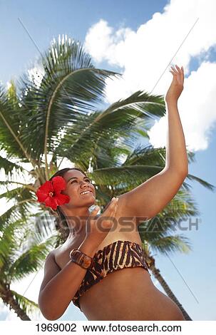 Stock Image - Hawaii, Oahu, Local Polynesian Hula Dancer Smiling And Dancing With Coconut Palm Trees In Background.. Fotosearch