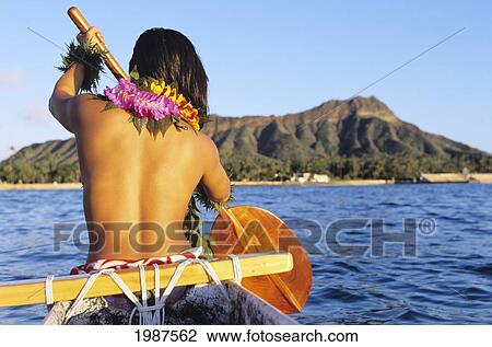 Stock Image - Hawaii, Oahu, Local Woman Paddling In Outrigger Canoe, Topless, View From Behind, Diamond Head In Distance. No Model Release. Fotosearch
