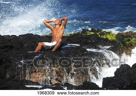 Stock Photo - Hawaii, Oahu, Local Young Man Enjoying Sea Mist On A Sunny Day On The Rocks On Shore.. Fotosearch