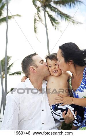 Stock Photograph - Hawaii, Oahu, Loving Moment Of Parents Kissing Their Young Son On His Cheeks.. Fotosearch