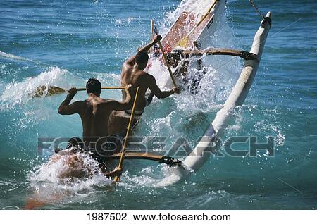Stock Image - Hawaii, Oahu, Makaha, Men's Paddling Team Surfing Shore Break, View From Behind. No Model Release. Fotosearch