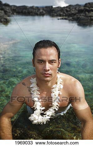 Stock Image - Hawaii, Oahu, Makapuu, Attractive Male Wearing A Lei Sitting In A Beautiful Tidepool. Fotosearch