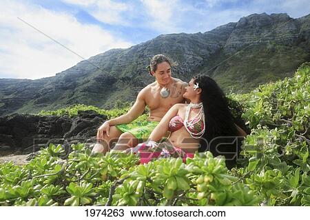 Stock Image - Hawaii, Oahu, Makapuu, Male And Female Hula Dancers Sit On The Shore. Fotosearch
