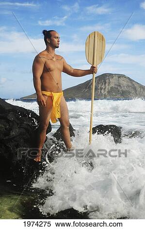 Stock Photography - Hawaii, Oahu, Makapuu, Polynesian Man In Traditional Hawaiian Clothing On Rocky Shore Holding A Paddle.. Fotosearch