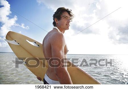 Stock Image - Hawaii, Oahu, Male Holding His Surfboard At The Beach.. Fotosearch