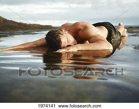 Stock Image - Hawaii, Oahu, Man Laying In Shallow Water On A Rocky Area.. Fotosearch
