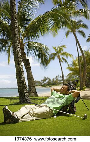 Stock Photograph - Hawaii, Oahu, Man Resting On Golf Course With Gear.. Fotosearch