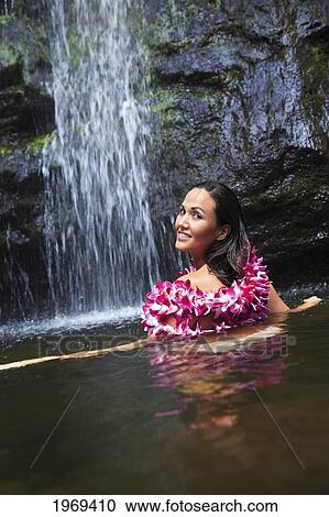 Stock Image - Hawaii, Oahu, Manoa Falls, Beautiful Female With Orchids Leis Sitting In A Pond At The Bottom Of Manoa Waterfalls.. Fotosearch