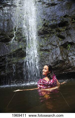 Stock Image - Hawaii, Oahu, Manoa Falls, Beautiful Female With Orchids Leis Sitting In A Pond At The Bottom Of Manoa Waterfalls.. Fotosearch