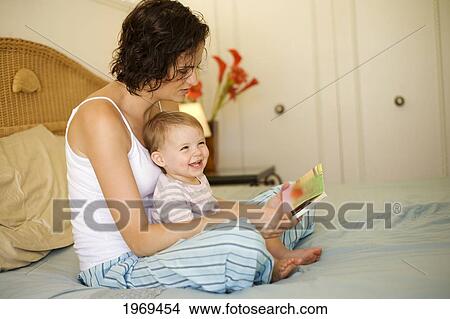 Picture - Hawaii, Oahu, Mother And Her Baby On The Bed Reading A Book.. Fotosearch