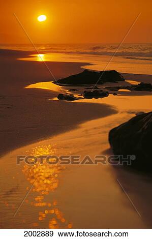 Stock Photo - Hawaii, Oahu, North Shore, Beautiful Orange Sunset On Rocky Shoreline, Reflections. Fotosearch